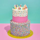 2 tier Birthday & Pinata Cake with rainbow sprinkles, colorful meringue drops, and vibrant sprinkle-covered base by Crumbs & Doilies.